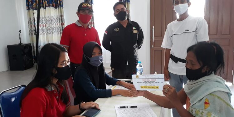 Sekdes Teluk Lawah, Samsudin (mengenakan topi) dan lainnya saat menyaksikan penyaluran BLT DD tahap V dan VI kepada masyarakat tidak mampu terdampak COVID-19, di gedung pertemuan desa setempat, Jumat (23/10/2020). (FOTO : PWI Gunung Mas)