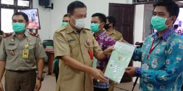 Sekda Gumas Yansiterson (tengah) didampingi Kepala BPN Gumas Ferdinan Adinoto (kiri) menyerahkan secara simbolis sertifikat hak atas tanah dari program PTSL ASN kepada warga, di Kuala Kurun, Senin (9/11/2020). (ANT/IST)