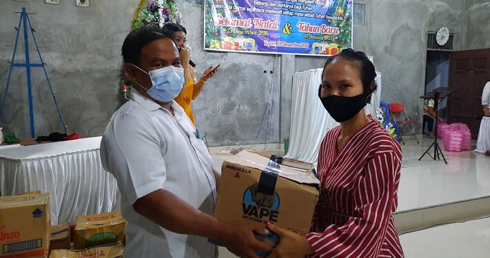 Penatua di Majelis Jemaat GKE Tuyun, Radius Prakarsa (kiri) menyerahkan bingkisan kasih secara simbolis kepada jemaat, usai pelaksanaan ibadah malam Natal di Gereja Efrata GKE Tuyun, Kamis (24/12/2020).