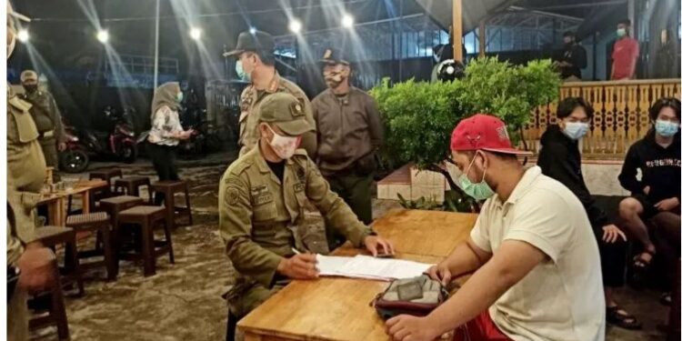 Petugas Satpol PP yang tergabung dalam Satgas COVID-19 Kabupaten Kapuas, memberikan edukasi dan sosialisasi tetang protokol kesehatan kepada salah satu pengunjung kafe di Kota Kuala Kapuas, Selasa, (22/12) malam. (ANT/IST)