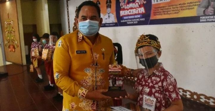 Kepala DPK Kabupaten Gumas Edwin Yustian menyerahkan trofi kepada Fernando Clean sebagai juara 1 lomba bercerita tingkat SD sederajat se-Gumas, di GPU Tampung Penyang, Kamis (29/4/2021). (ANT/IST)