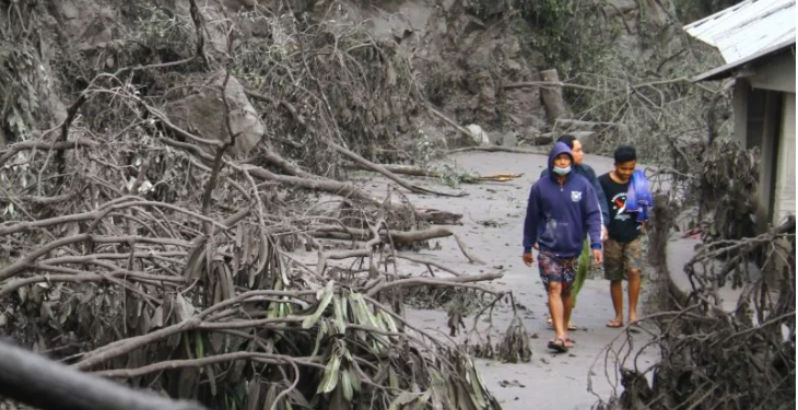 Dua orang pejalan kaki melintasi jalur Malang-Lumajang yang terhalang batang pepohonan yang roboh di Pronojiwo, Lumajang, Jawa Timur, Minggu (5/12/2021). Derasnya guyuran hujan abu vulkanik akibat erupsi gunung Semeru membuat pohon di sepanjang jalur tersebut roboh dan menghalangi jalan. (IST)