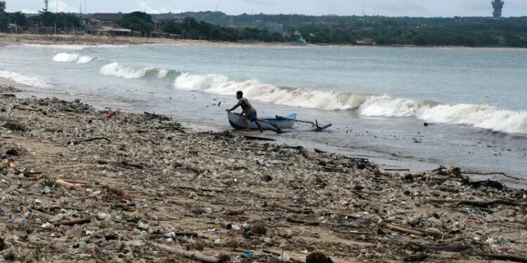 Nelayan beraktivitas di dekat tumpukan sampah yang berserakan di Pantai Kedonganan, Badung, Bali, Selasa (7/12/2021). Cuaca ekstrem yang melanda Bali pada Senin (6/12/2021) tersebut menyebabkan sampah plastik, kayu, bambu dan kelapa terdampar di pesisir pantai akibat terbawa gelombang laut sehingga mencemari kawasan pariwisata itu. (MASAPNEWS/ANT)