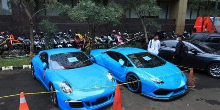 Petugas kepolisian melihat barang sitaan milik tersangka kasus dugaan penipuan investasi trading binary option lewat aplikasi Quotex Doni Salmanan di halaman Bareskrim Polri, Jakarta, Senin (14/3/2022). (MASAPNEWS/ANT)