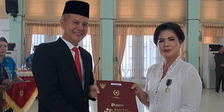 Bupati Gumas, Jaya S Monong (kiri) menyampaikan penghargaan Satyalancana Karya Satya dari Presiden RI kepada Kepala SDN 1 Kuala Kurun, Desmilawati, di GPU Damang Batu Kuala Kurun, Jumat (28/10/2022). (IST)