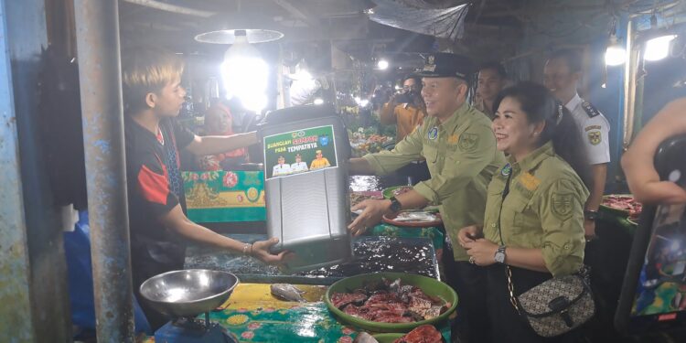 Bupati Gunung Mas Jaya S Monong, didampingi Ketua FKGMS Mimie Mariatie dan Camat Kurun Iltem, membagikan tempat sampah kepada salah satu pedagang di Pasar Lama Kuala Kurun, Kecamatan Kurun, Rabu (29/11/2023). (MASAPNEWS/GCM)