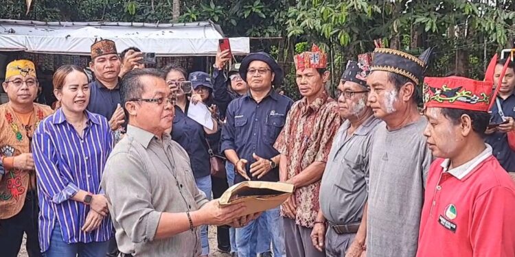 Legislator Kabupaten Gunung Mas Nomi Aprilia (baju garis-garis) mendampingi Asisten III Setda Gumas Letus Guntur saat penyerahan bantuan program pokir untuk pelaksanaan Tiwah massal di Kelurahan Tampang Tumbang Anjir Kecamatan Kurun, Sabtu (8/5/2024). (MASAPNEWS/GCM)