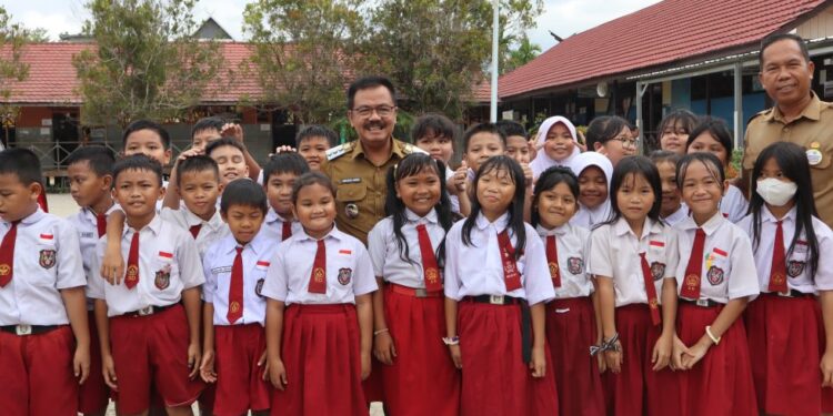 Pj Bupati Gumas Herson B Aden, Kepala SDN 3 Kuala Kurun Belie, berfoto bersama peserta didik di SD setempat, Senin (15/7/2024). (Foto : Diskominfosantik Gumas)